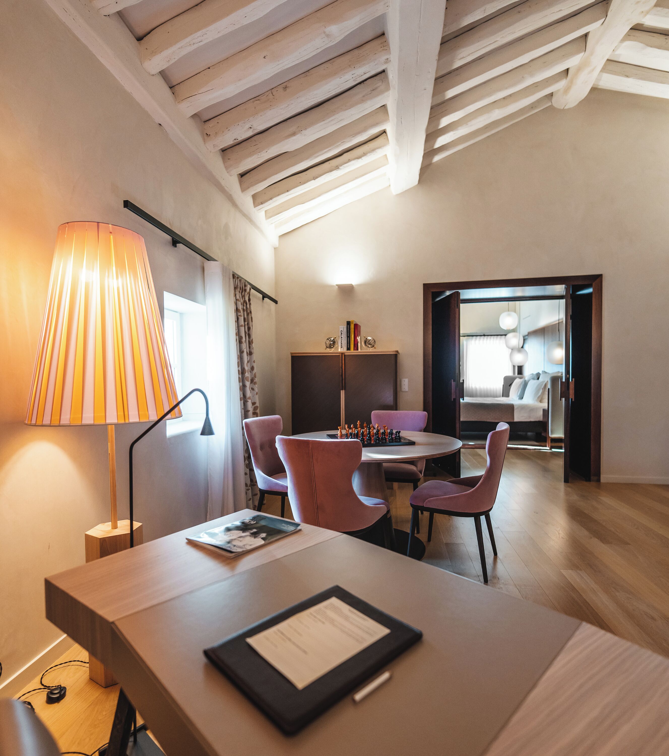 A modern room with a wooden ceiling, a dining table with pink chairs, a lamp, and a chessboard.