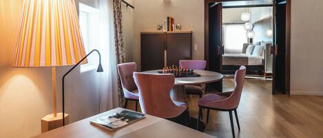 A modern room with a wooden ceiling, a dining table with pink chairs, a lamp, and a chessboard.