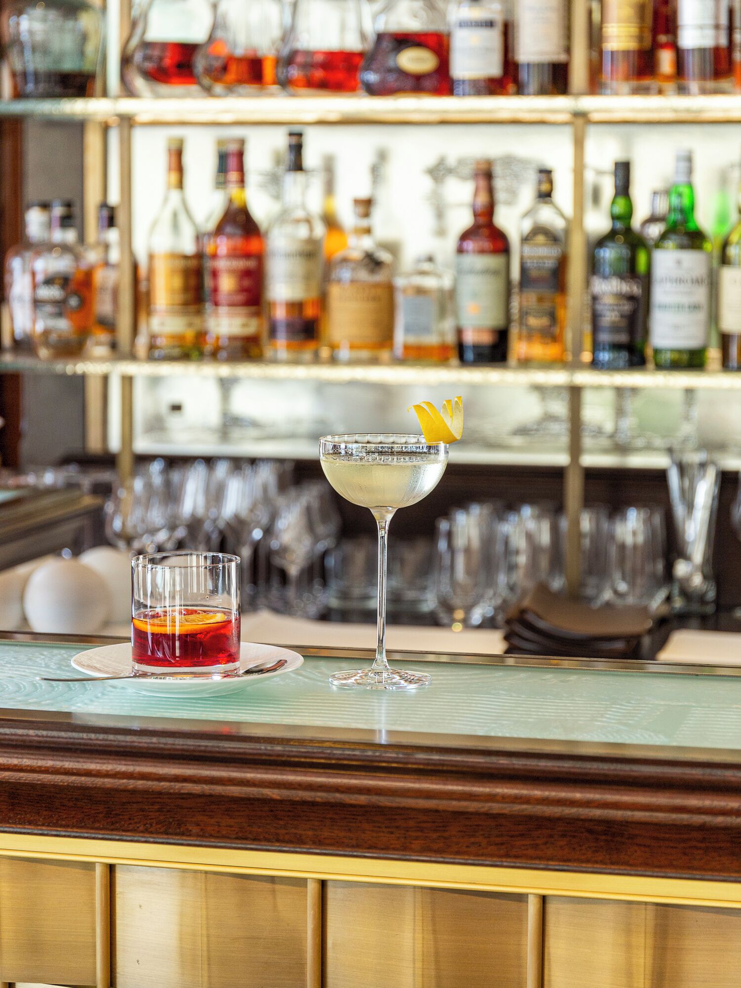 A bar area with a variety of liquor bottles on shelves and two glasses of drinks on the counter.