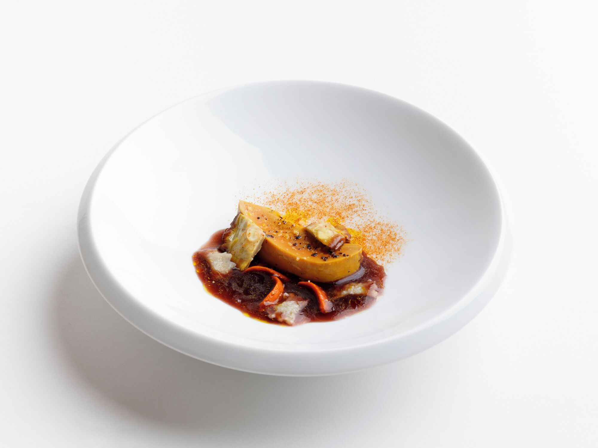 Une assiette blanche contenant un dessert composé d’un morceau de fruit, d’une cuillerée de crème et d’une pincée d’épices.