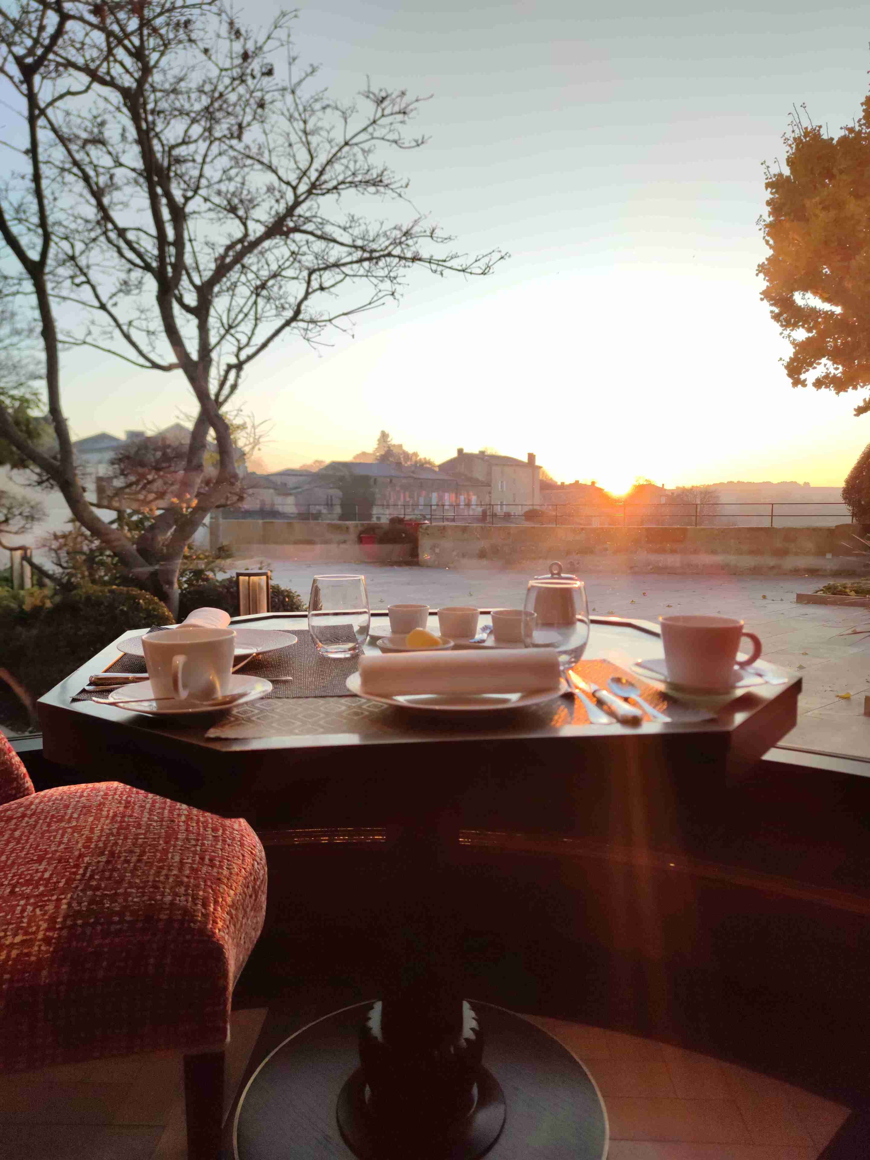 Una mesa dispuesta para el desayuno, con vista a un atardecer y edificios al fondo.