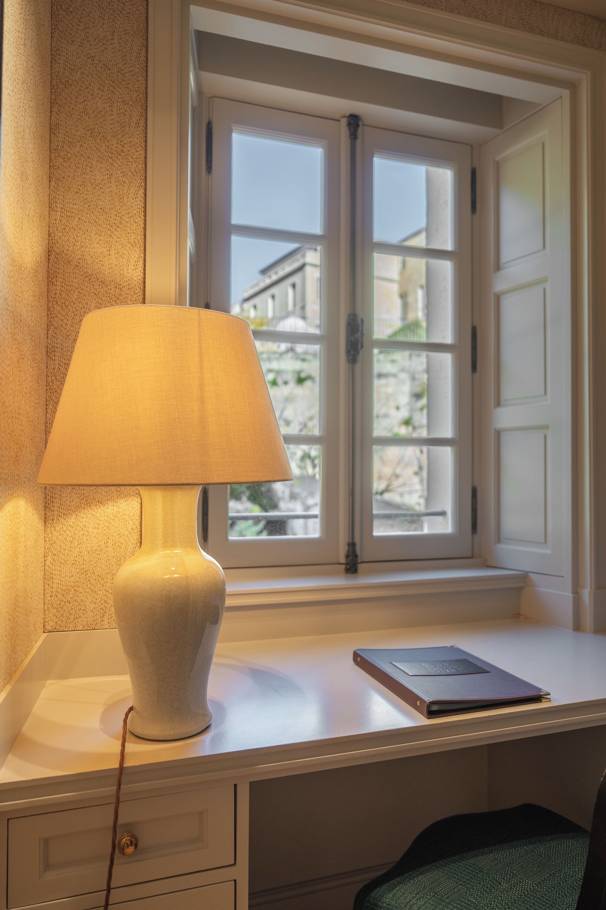 A desk with a lamp, a book, and a window with a view of buildings.