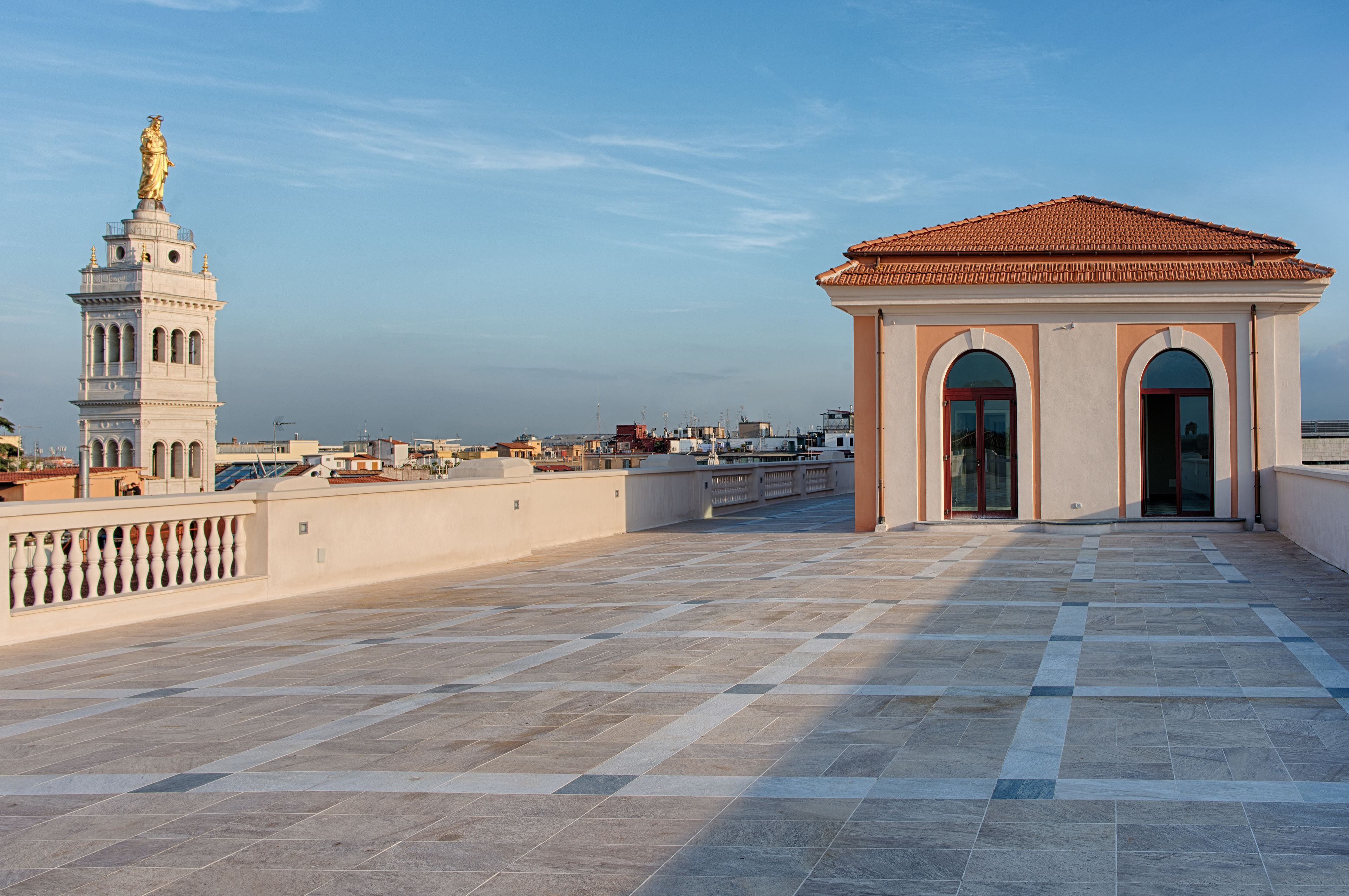 A spacious rooftop terrace with a tiled floor, a statue, and a building with arched windows.