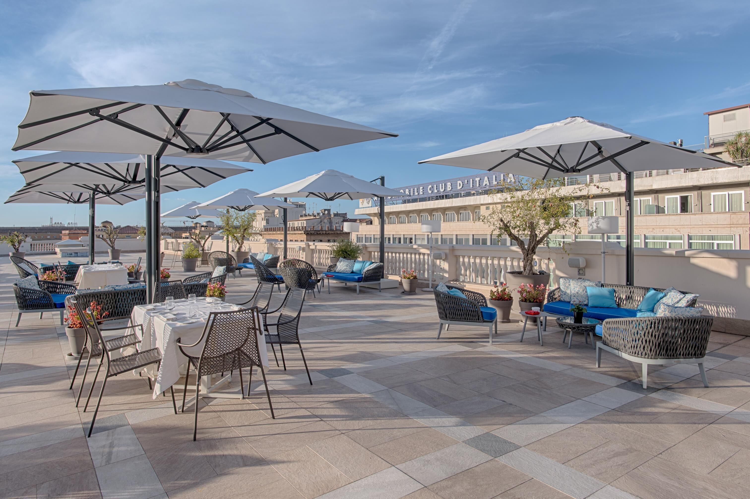 Eine Außenpatio-Terrasse mit Tischen, Stühlen und Sonnenschirmen, mit Blick auf das Hotel im Hintergrund.