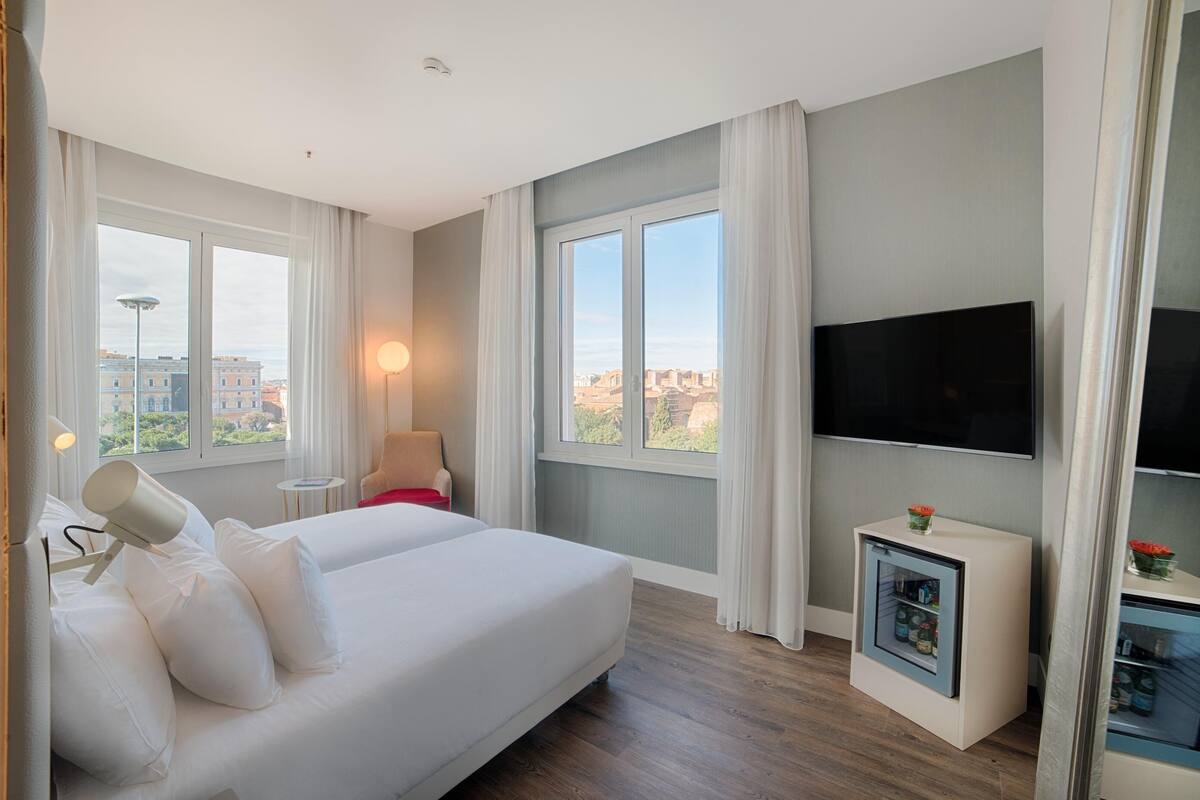 A hotel room with a bed, a TV, a small table, and a minibar.