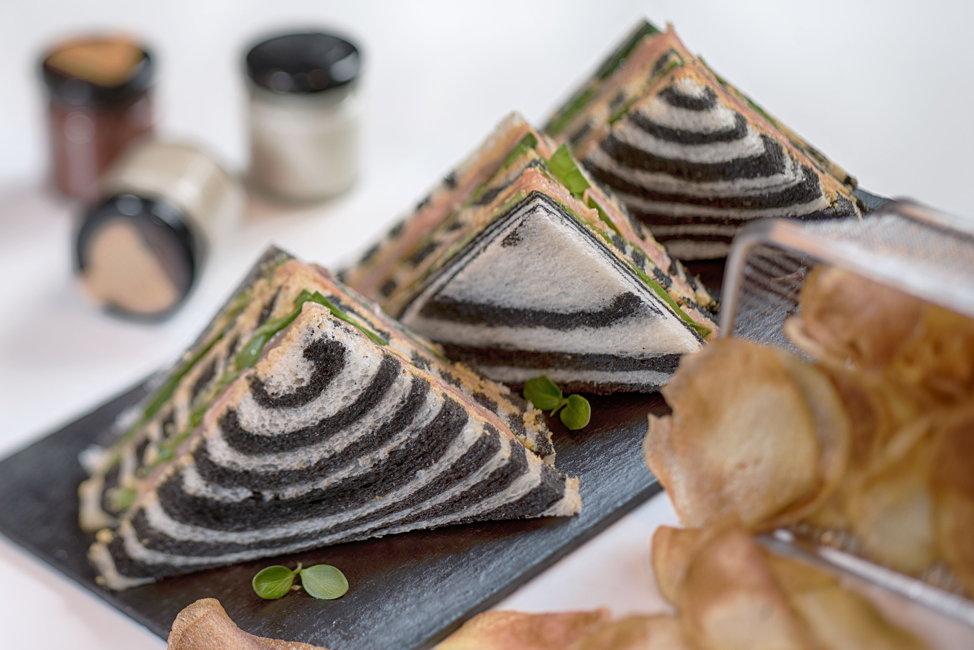 A tray of layered pastries on a dark slate board, accompanied by small green leaves and a knife.
