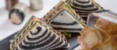 A tray of layered pastries on a dark slate board, accompanied by small green leaves and a knife.