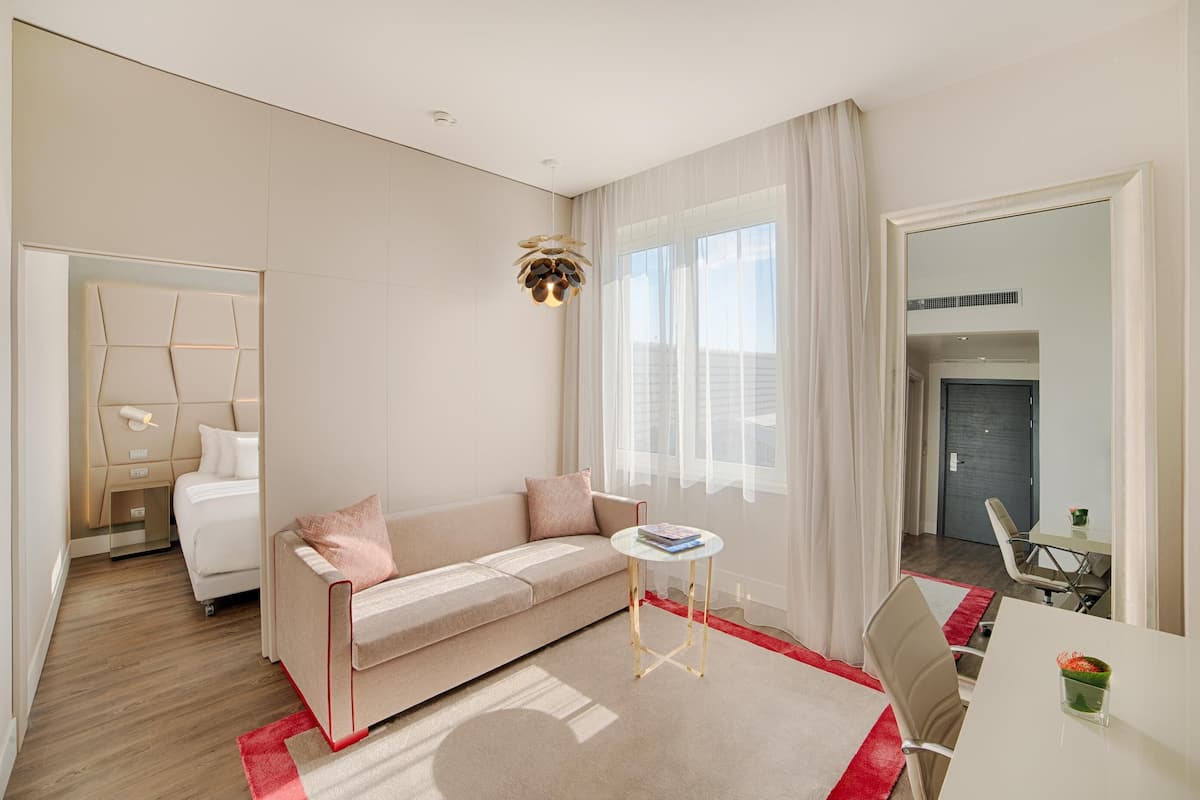 A modern hotel room with a sofa, a small round table, a mirror, and a view of the city.