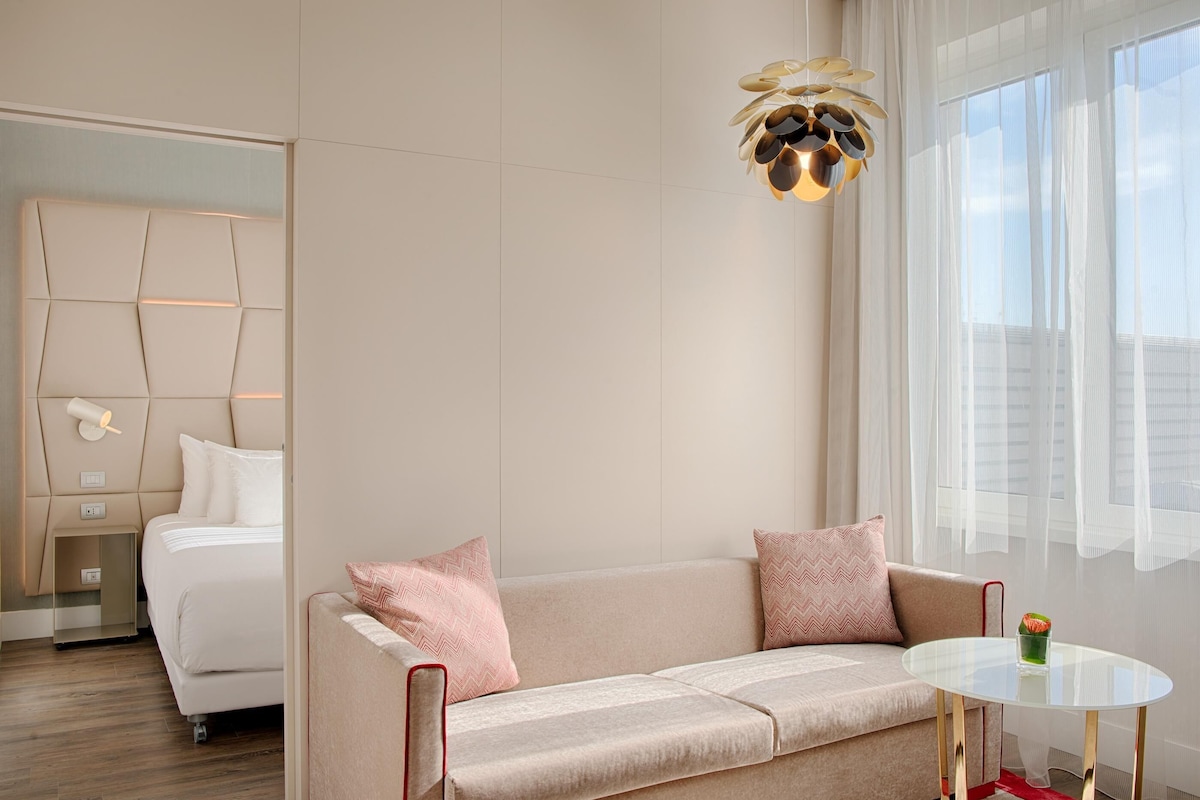A modern hotel room with a sofa, a glass table, and a decorative light fixture.