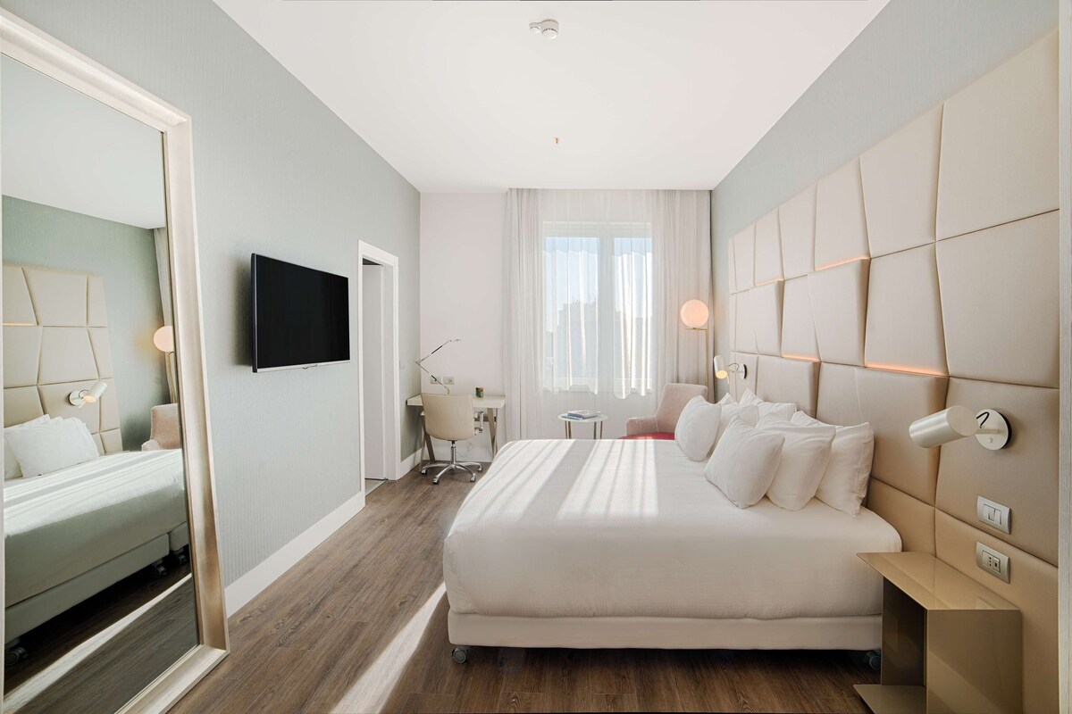A modern hotel room with a large bed, a desk, and a television.