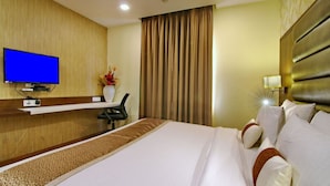 Ein Hotelzimmer mit einem großen Bett, einem flachbildfernseher an der Wand, einem Schreibtisch mit Stuhl und einem Fenster mit Vorhängen.