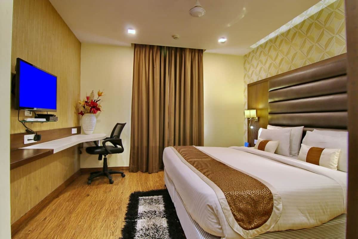 A hotel room with a bed, a desk with a computer, a TV, and a window with curtains.