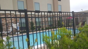 A pool area with a black fence, lounge chairs, and a building with stone facade and windows.