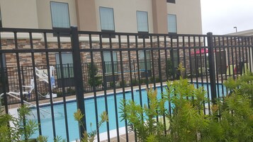 Zona de piscina con cerramiento negro, sillas de descanso y un edificio con fachada de piedra y ventanas.