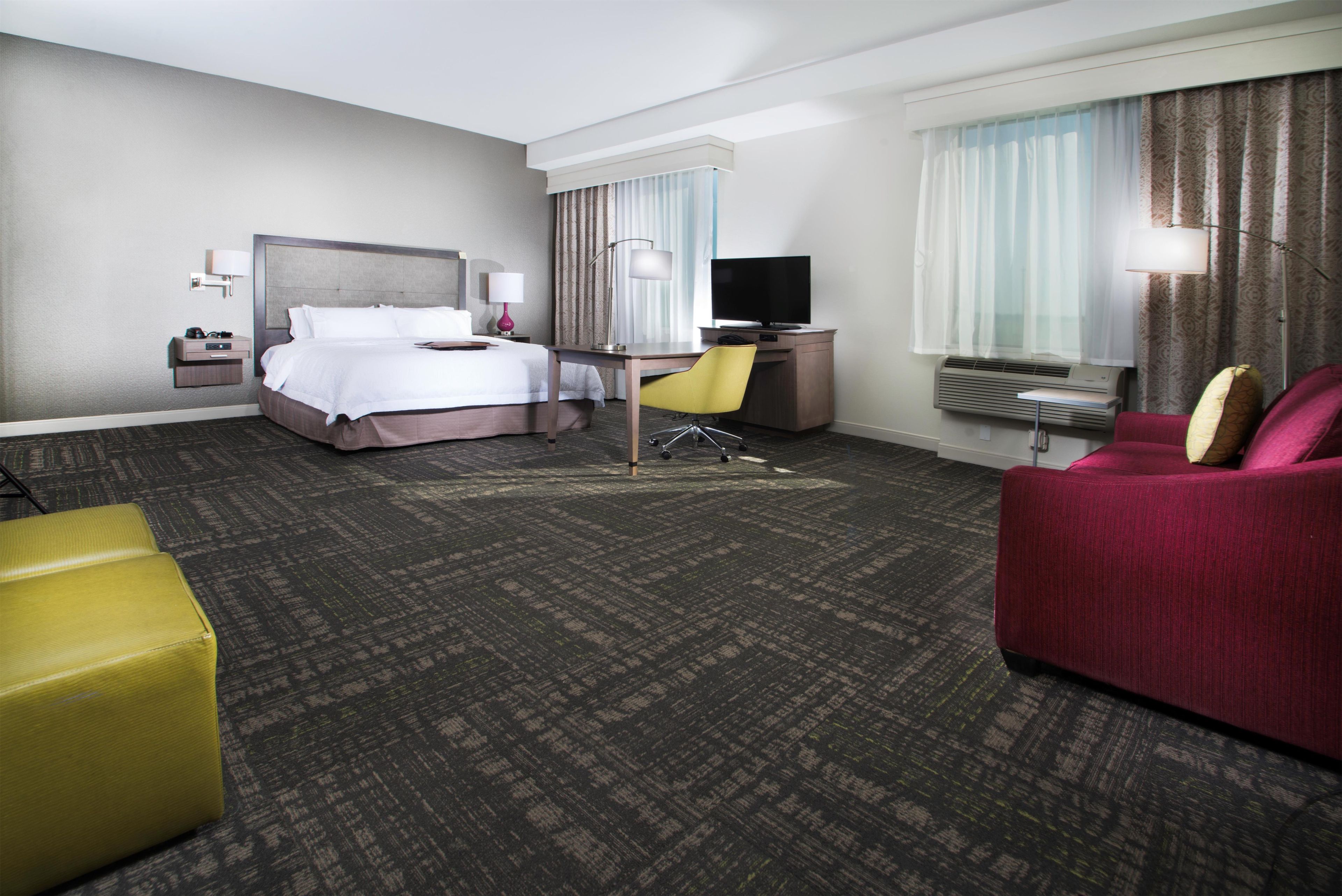 A hotel room with a bed, desk, chair, television, and a sofa.