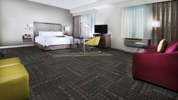 A hotel room with a bed, desk, chair, television, and a sofa.