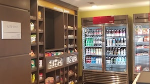 A hotel suite shop with shelves stocked with snacks and beverages, a refrigerated display case, and a sign indicating 24-hour availability. - Hampton Inn & Suites La Porte (La Porte)
