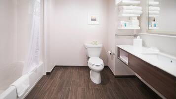 Un bagno con il water, una vasca, un lavabo con uno specchio e uno scaffale con asciugamani.