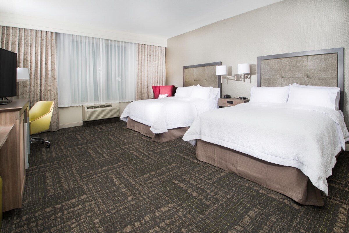 A hotel room with two beds, a desk, a chair, and a television.