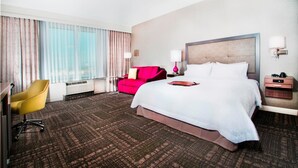 A hotel room with a large bed, a red sofa, a yellow chair, and a desk.