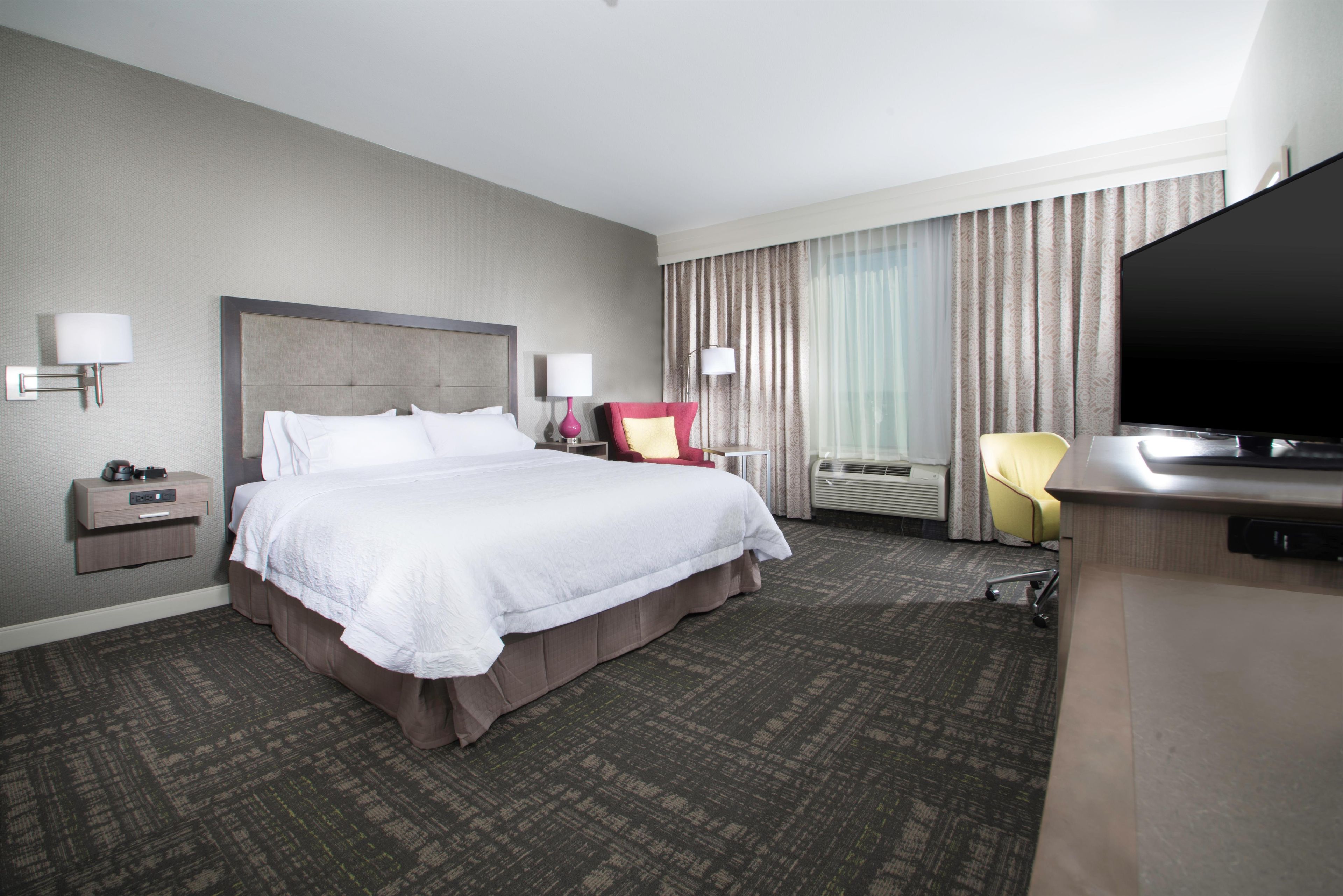 A hotel room with a large bed, a desk, a chair, a flat-screen TV, and a window with curtains.
