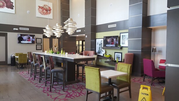 A modern hotel lobby with a long reception desk, multiple seating areas, and a large chandelier.