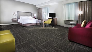 Una habitación de hotel con cama, escritorio, silla, televisor y sofá.