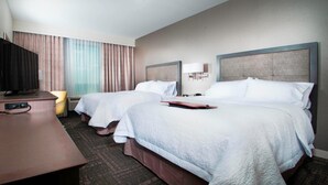 A hotel room with two beds, a desk with a TV, and a chair.