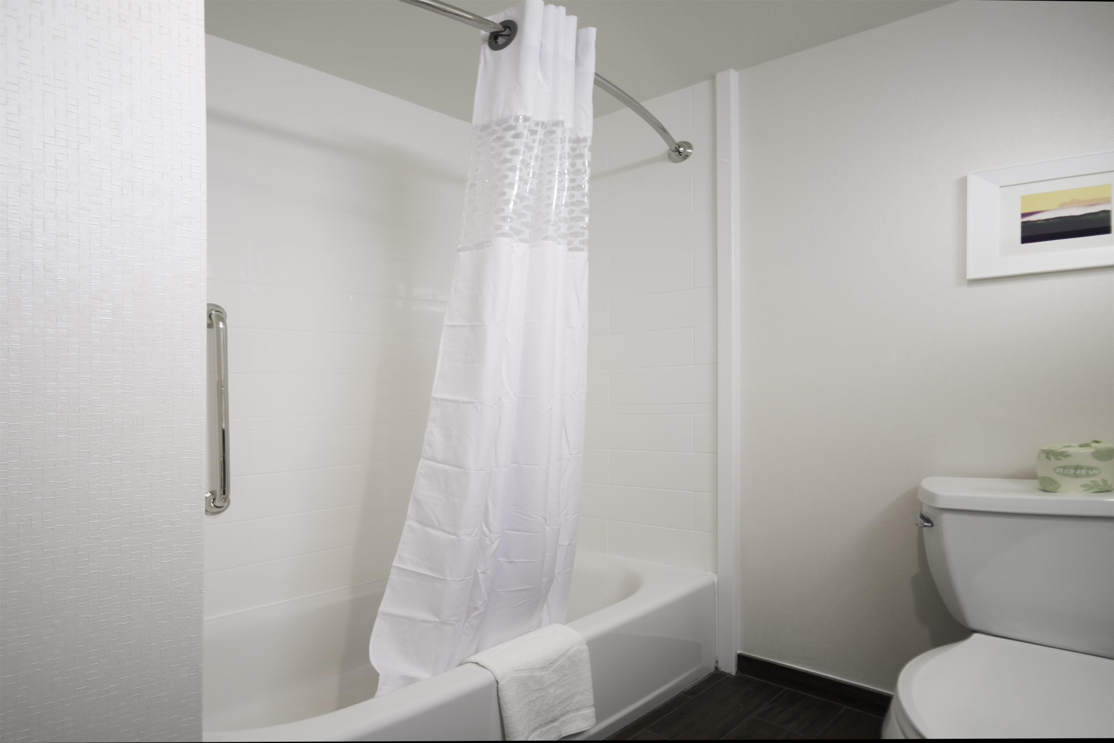 A bathroom with a white bathtub, a shower curtain, and a toilet.