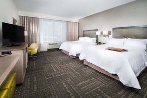Ein Hotelzimmer mit zwei Betten, einem Fernseher, einem Schreibtisch und einem Sessel.