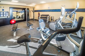 Ein Fitnessstudio mit verschiedenen Trainingsgeräten, darunter Laufbändern, einer Bank und Kurzhanteln.