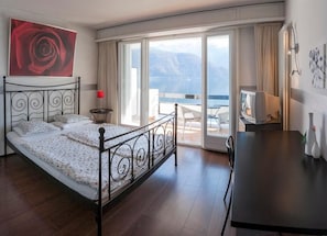 Quarto com cama, TV, escrivaninha e varanda com vista.