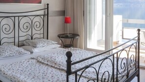 A bedroom with a bed, a small table, a TV, and a balcony with a view. - Hotel Garni Battello (Melide)