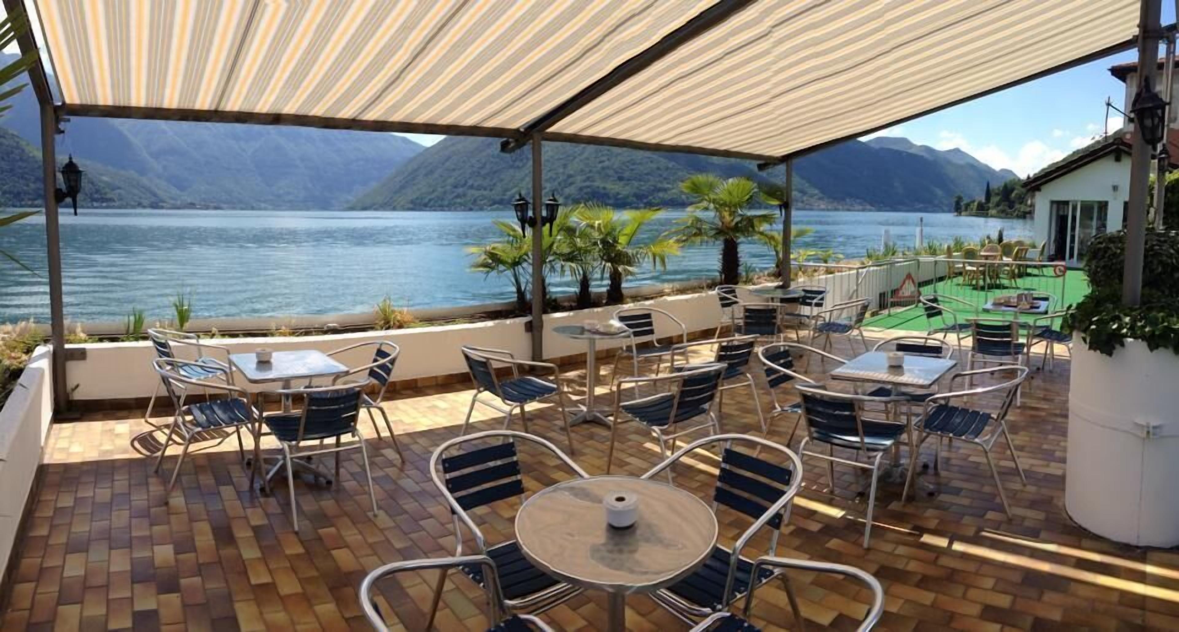 Une terrasse extérieure avec des tables et des chaises, offrant une vue sur un lac et des montagnes.