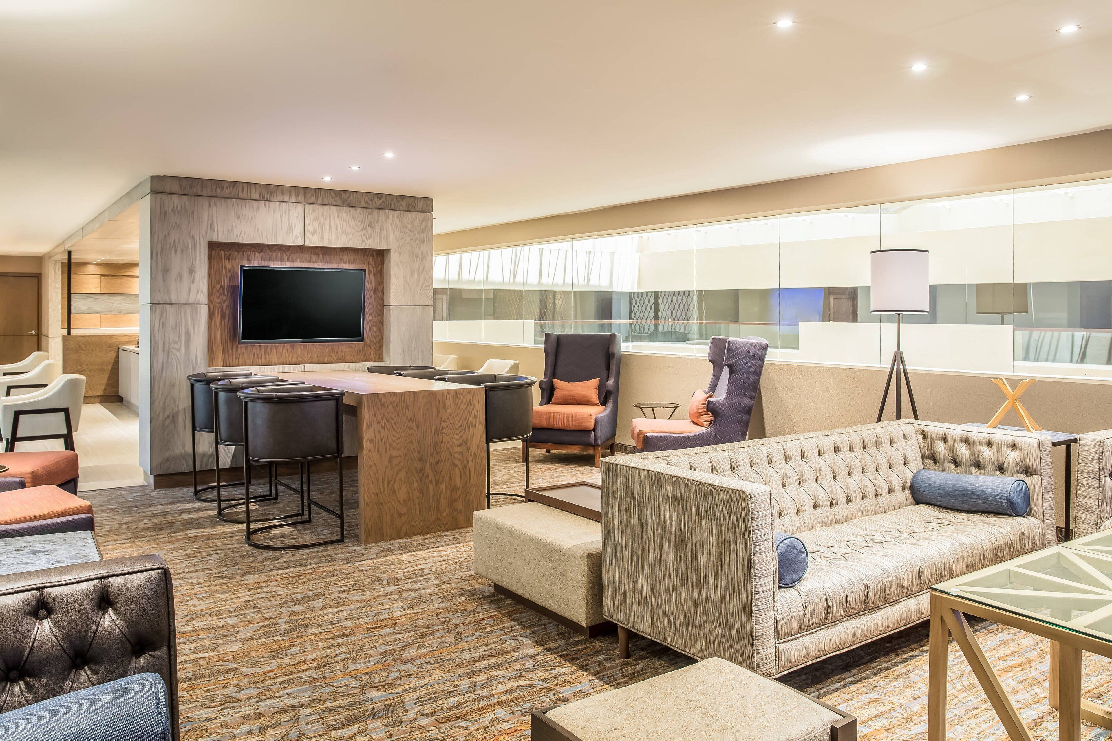Un hall d’hôtel moderne doté d’un bar, de différents espaces de détente et d’un grand écran de télévision.