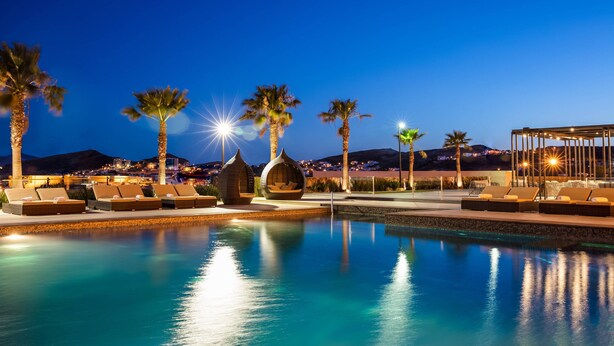 Zona de piscina con sillas de descanso y palmeras al anochecer.