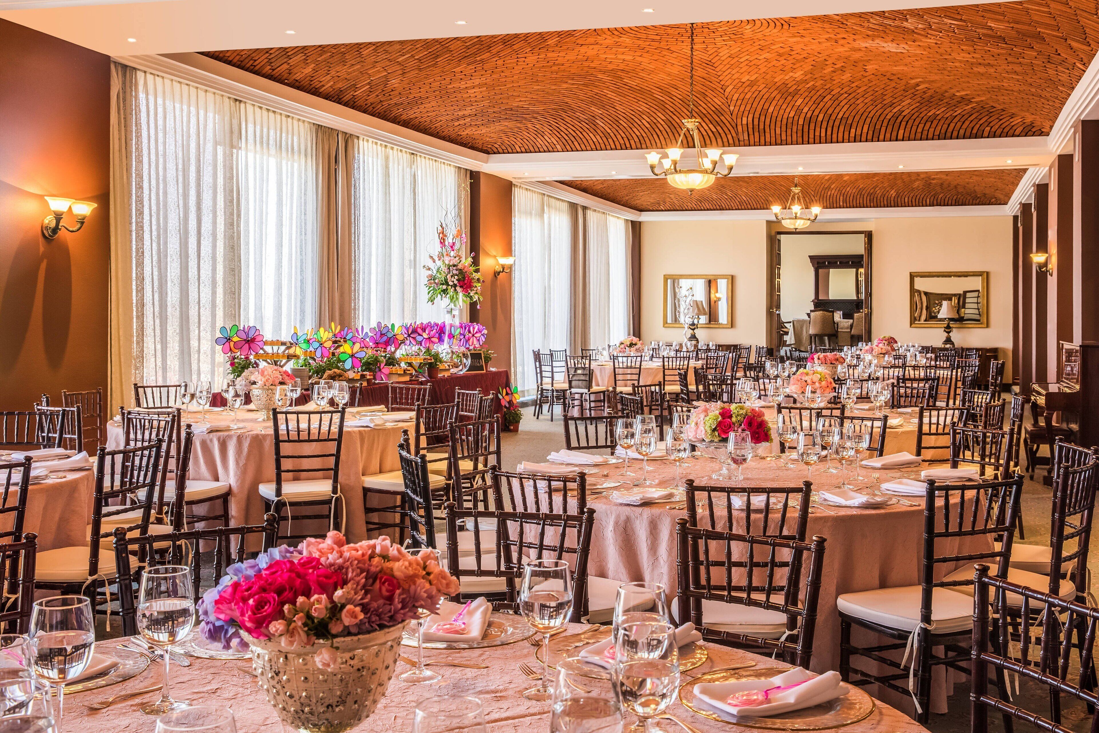 A banquet hall with round tables set for dining, wooden chairs, and floral centerpieces.
