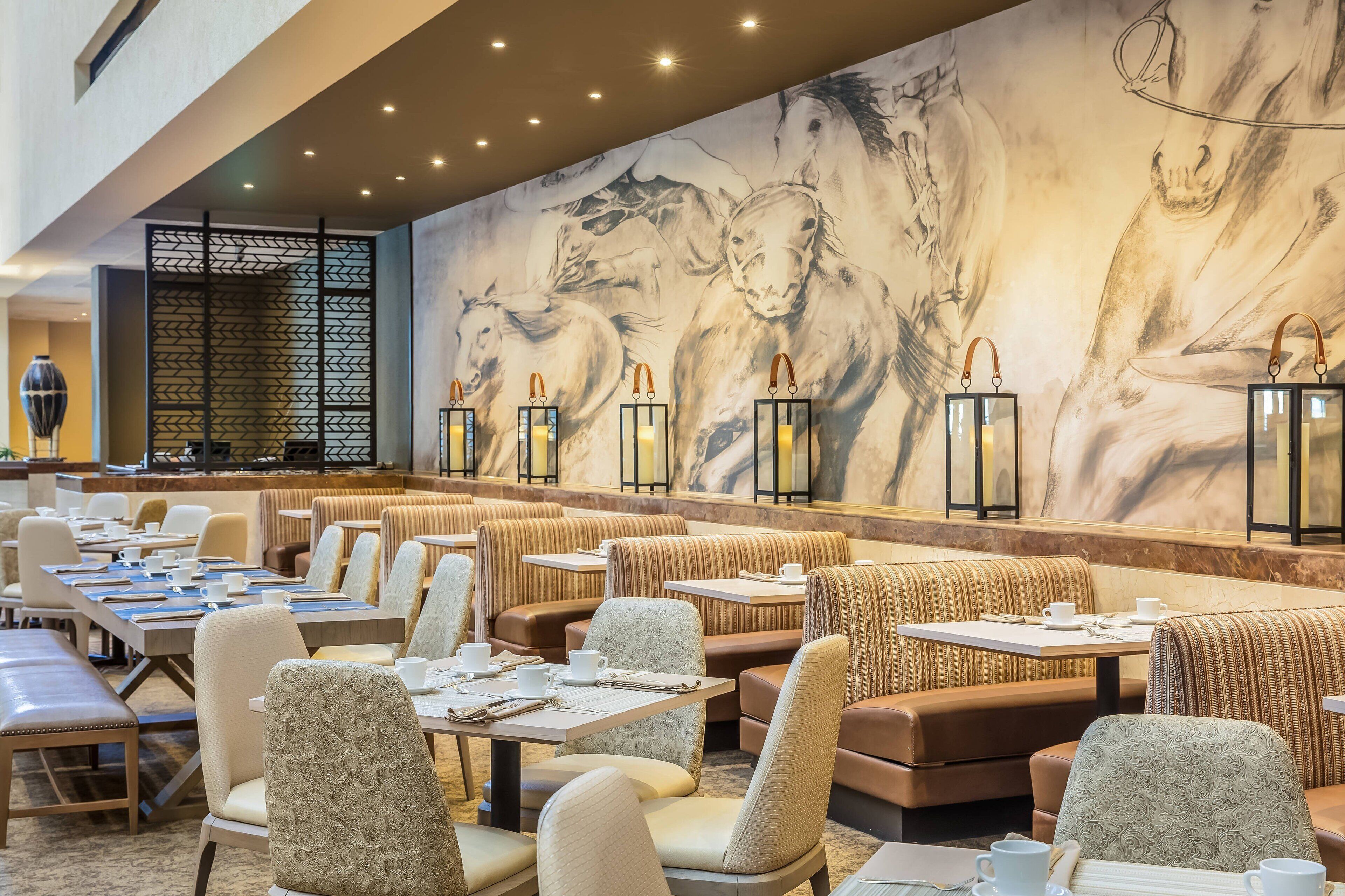 Un restaurant amb seients en cabines i taules, un mural gran de cavalls i llanternes penjants.
