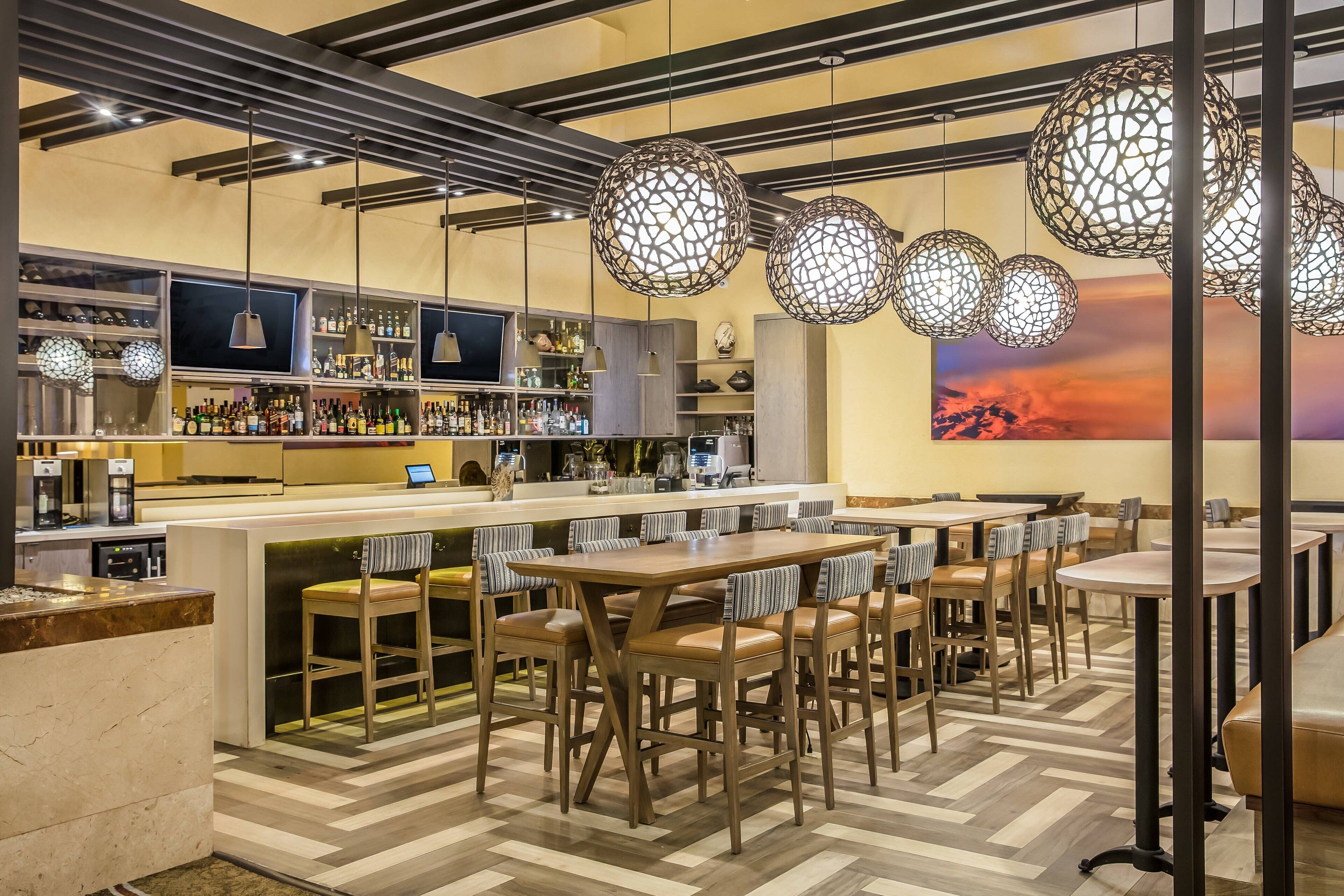 Un'area bar con un lungo bancone, diverse disposizioni di posti a sedere e lampade sferiche a sospensione.