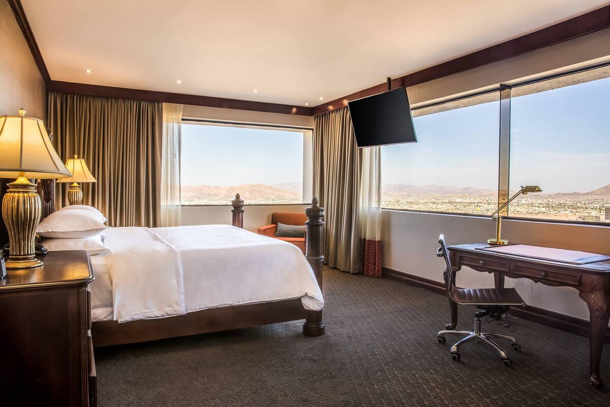 A hotel room with a large bed, a desk, a chair, and a TV.