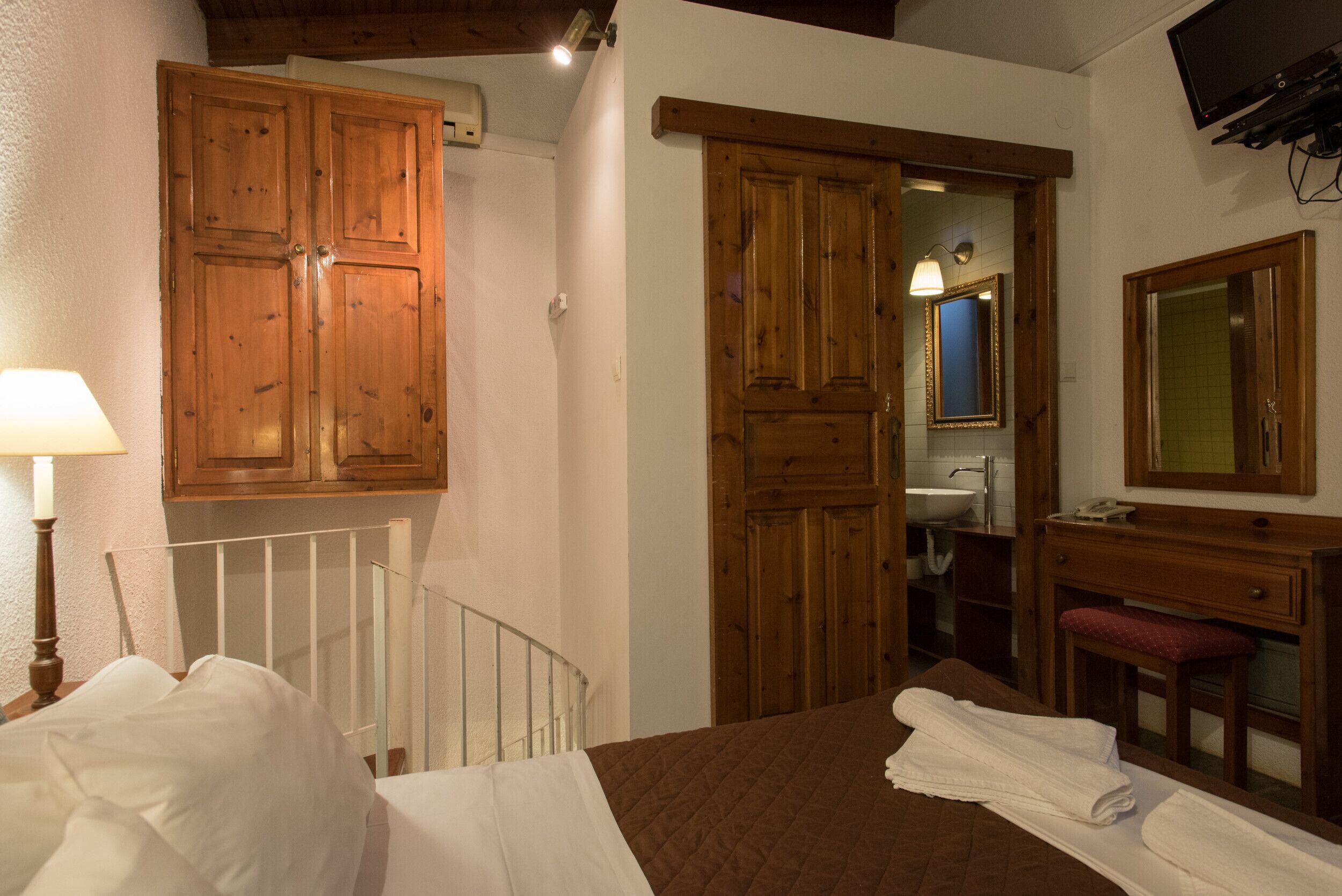 Une chambre à coucher avec un lit, une armoire en bois et une salle de bain visible à travers une porte ouverte.