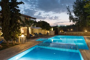 A swimming pool with a stone deck, lounge chairs, and a covered seating area. - Proimos Maisonnettes (Platanias)
