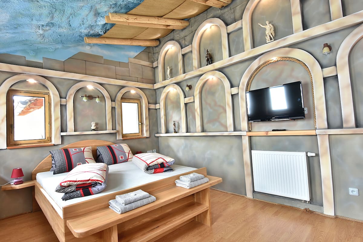 A bedroom with a bed, bedside tables, a TV, and a window.