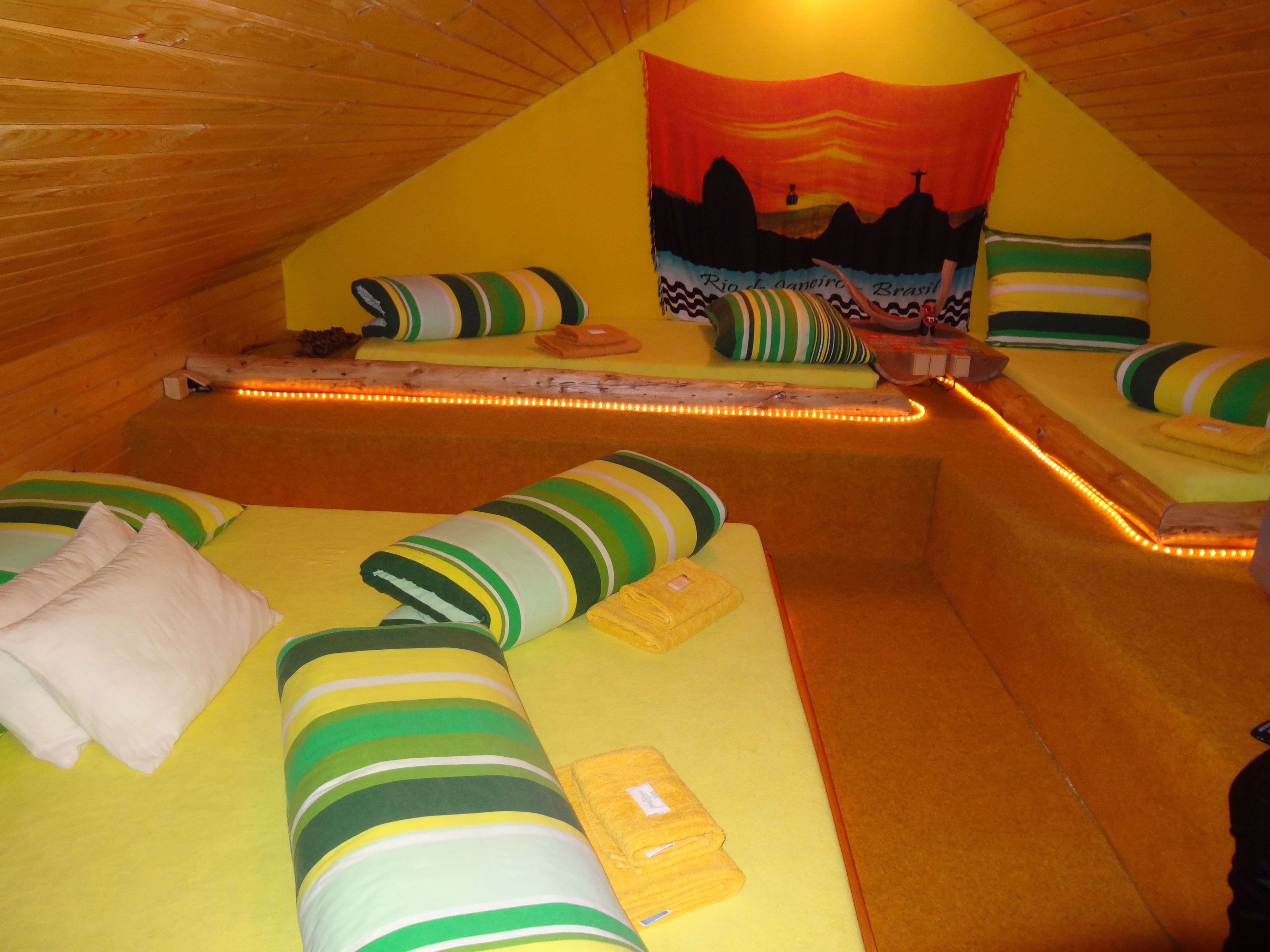 Een knus, driehoekig vertrek met schuine wanden, met een bed met gestreepte beddengoed en een kleurrijk wandtapijt waarop een Braziliaans landschap te zien is.