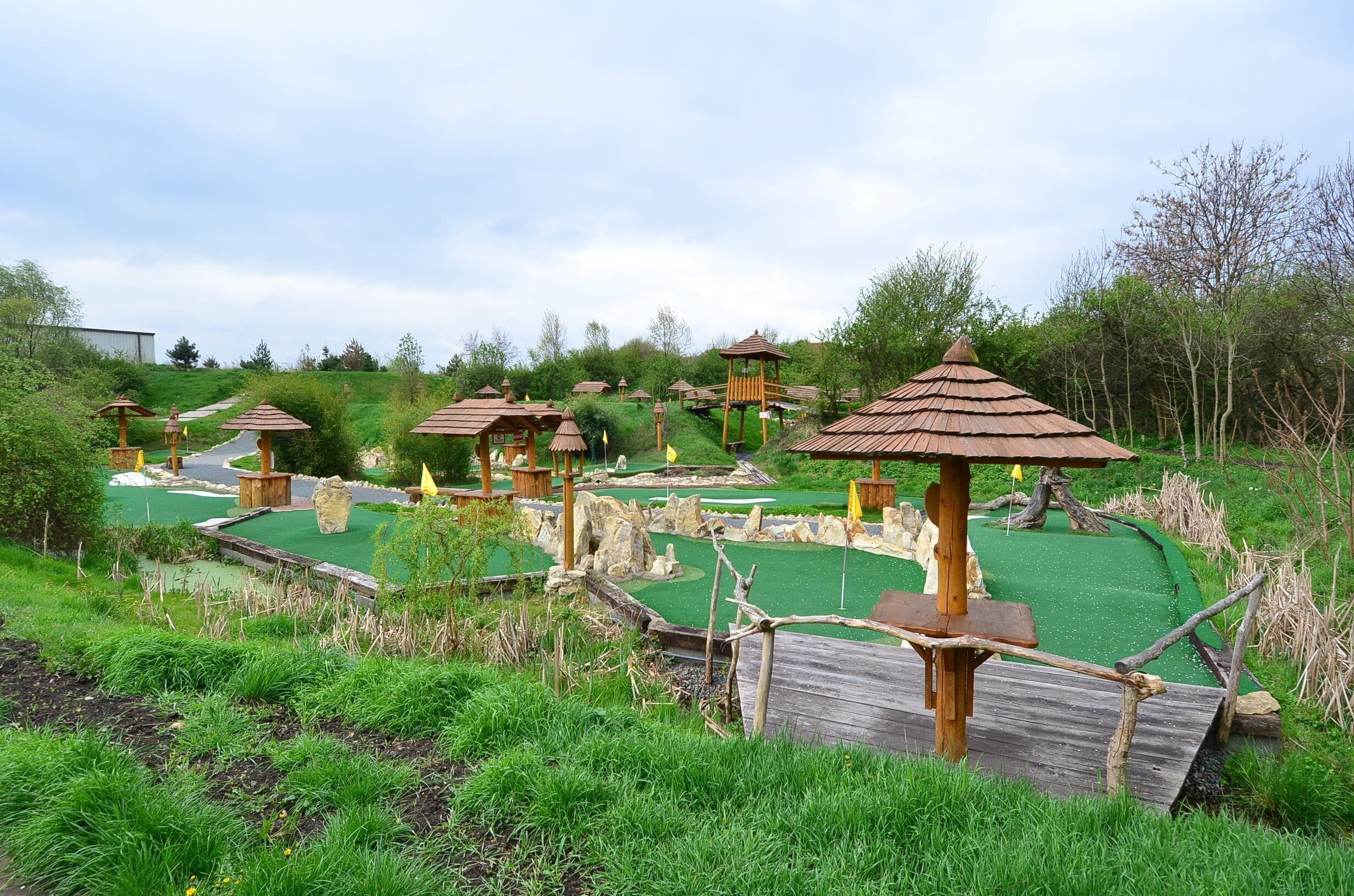 Ein Golfplatz mit mehreren Abschlagboxen, jede mit einer Holzhütte und einem Strohdach.