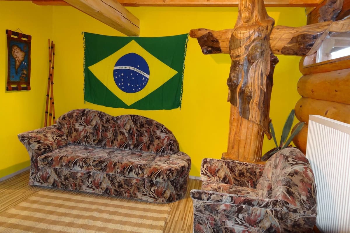 A room with a sofa, a wooden sculpture, a Brazilian flag, and a map on the wall.