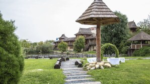 Un sendero conduce a un pabellón de madera en un exuberante jardín, con edificios tradicionales al fondo.