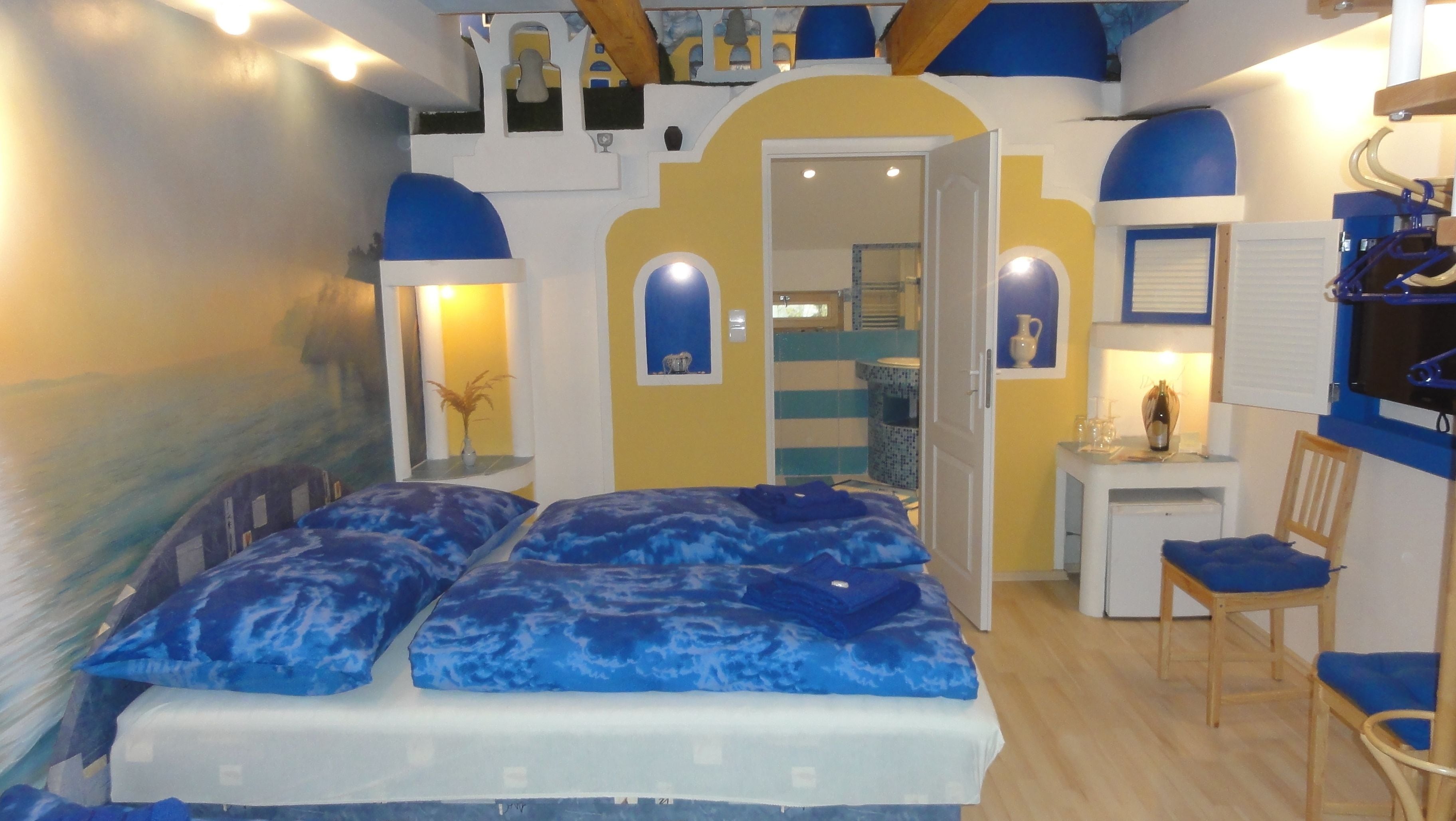 A room with a bed, a desk, and a chair. There is a door leading to another room.