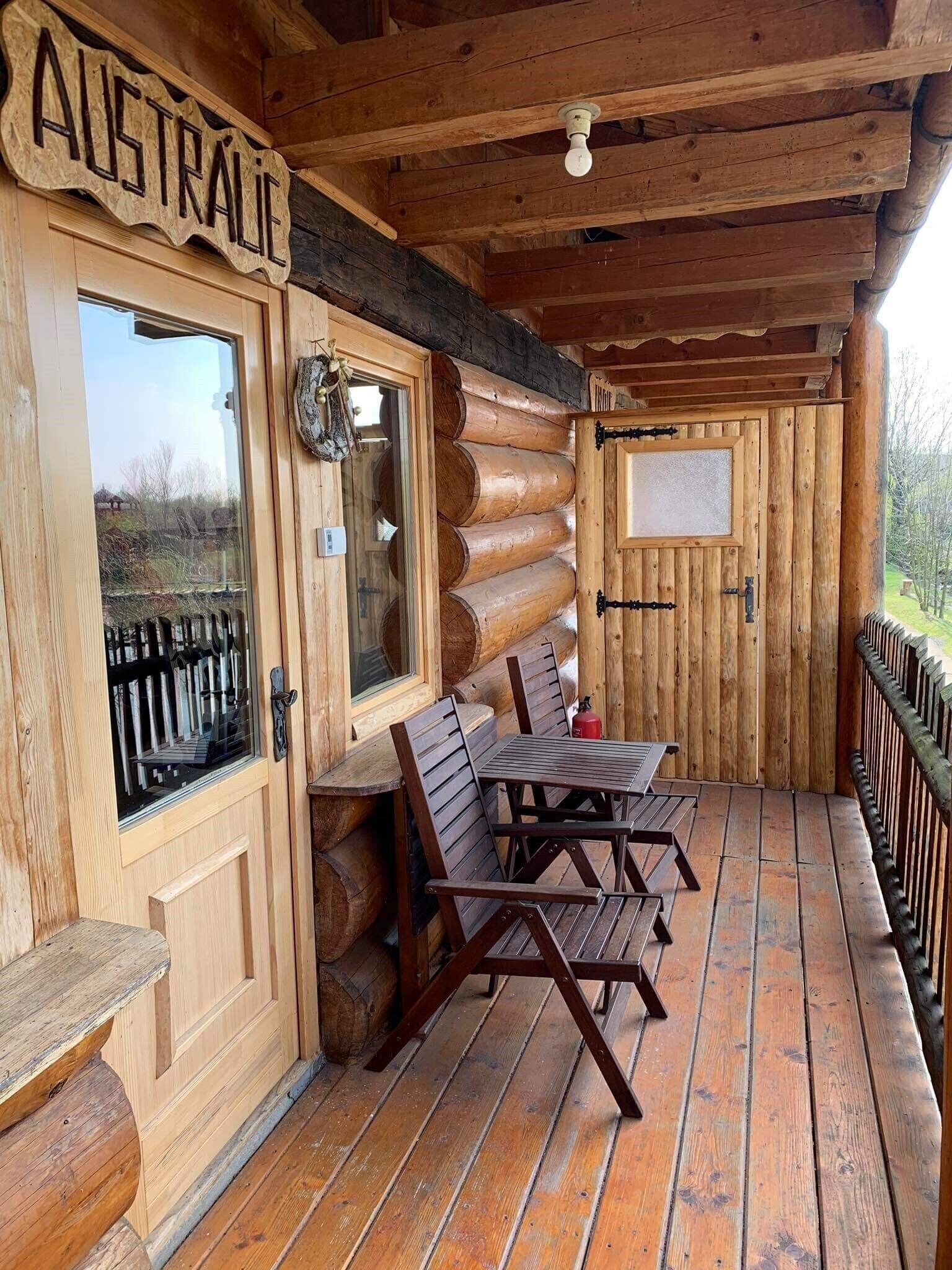 A wooden log cabin with a sign reading "AUSTRALIE" above the door, a wooden table with chairs, and a window with a view of the outside.