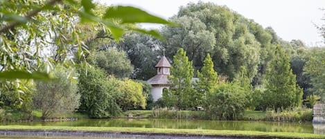 A serene park with a small building surrounded by lush greenery and a calm pond.